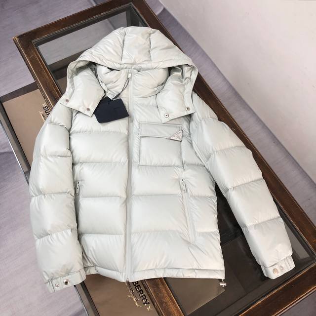 PRADA 普拉达 2024秋冬最新款亮面羽绒服！前胸口袋饰有品牌独特△三角金属铁标徽章 甄选客供100%棉纶材质制作而成，面料拥有极为优越的防水透气性，能抵挡