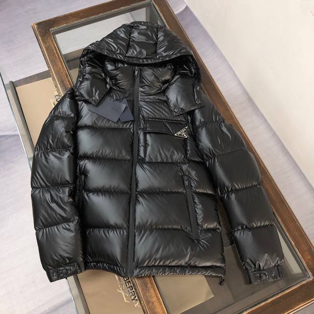 PRADA 普拉达 2024秋冬最新款亮面羽绒服！前胸口袋饰有品牌独特△三角金属铁标徽章 甄选客供100%棉纶材质制作而成，面料拥有极为优越的防水透气性，能抵挡